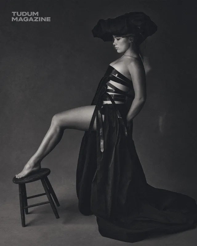 Florence Pugh posing in a black dress with one heel resting on a stool.