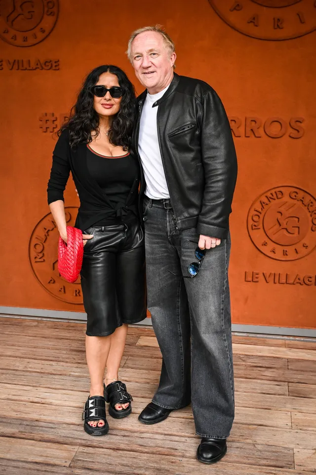 Salma Hayek posing at an event in a black outfit and sandals.