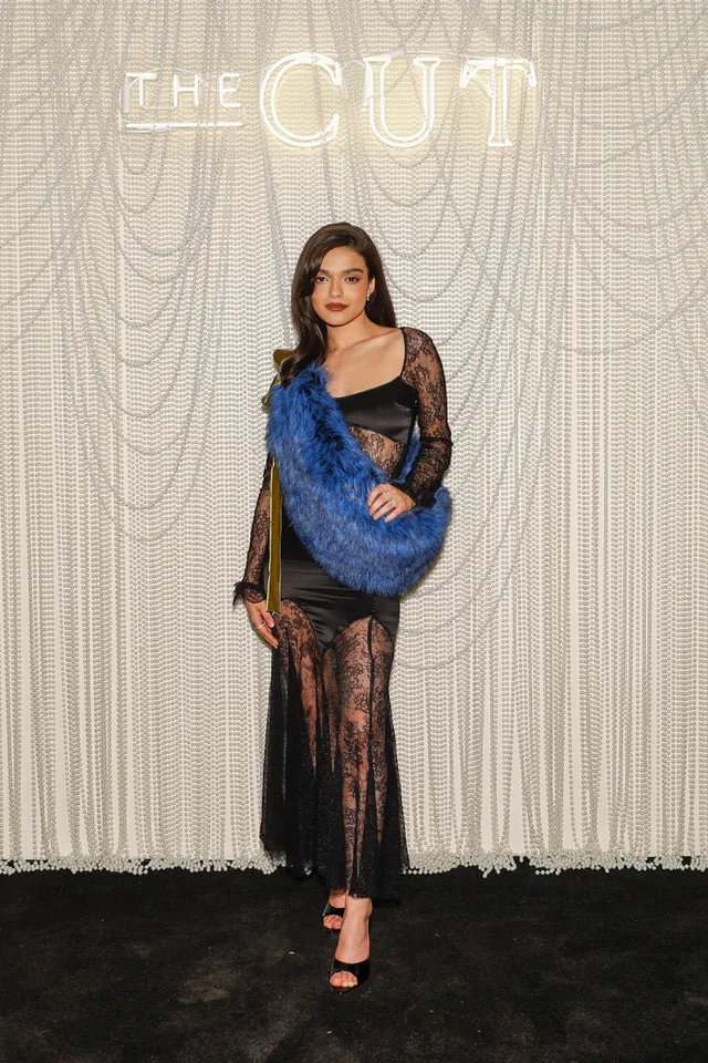 Rachel Zegler posing in a sheer black dress, blue wrap and heels.