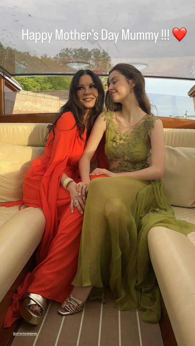 Catherine Zeta-Jones sitting beside another woman in a red dress and heels.