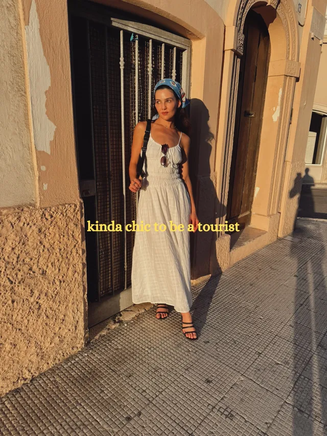 Danielle Campbell standing outdoors in a pale dress and sandals.