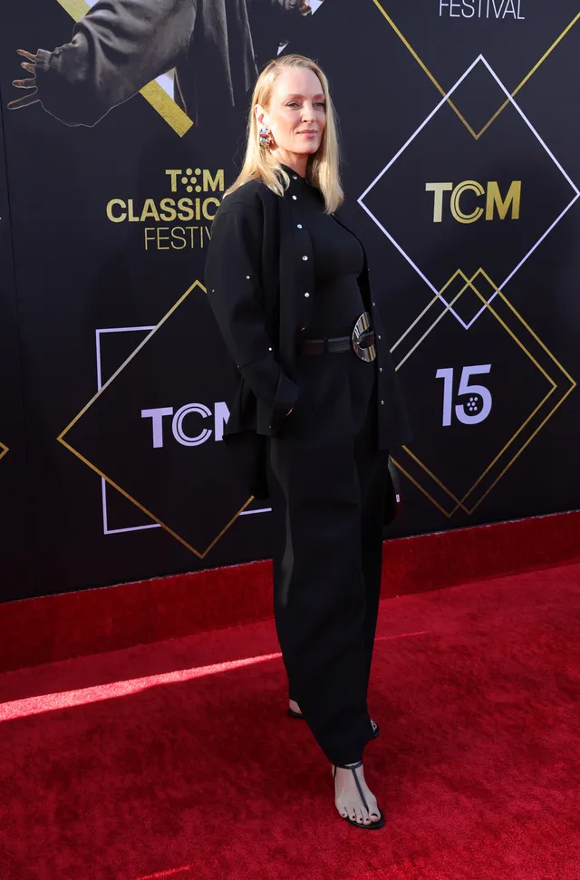 Uma Thurman wearing a black outfit and heels on a red carpet.