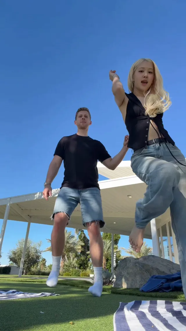 Rosé dancing on a lawn in blue jeans with one bare foot lifted.