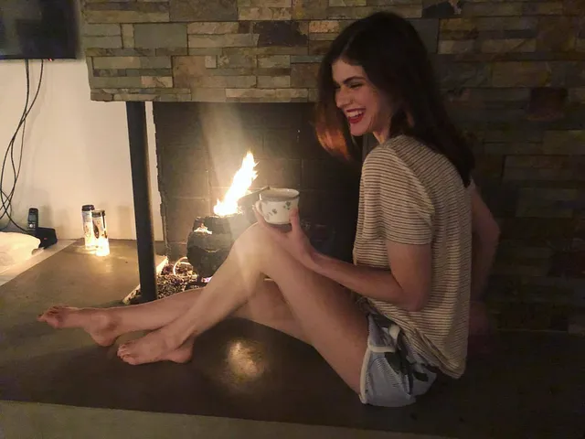 Alexandra Daddario seated beside a bathroom counter with a bare foot resting in front of her.