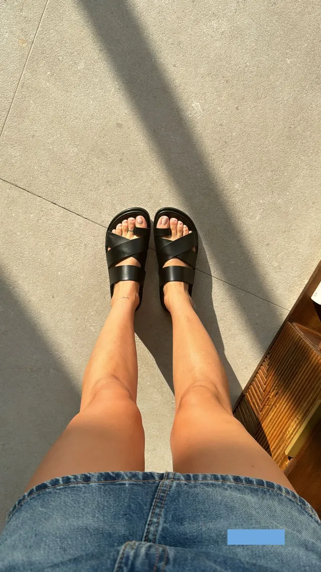 María Pedraza shown from above wearing denim shorts and dark flat sandals.