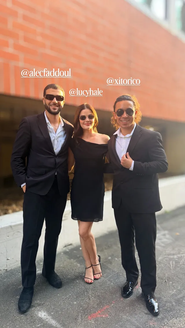 Lucy Hale posing with companions outside a brick building.