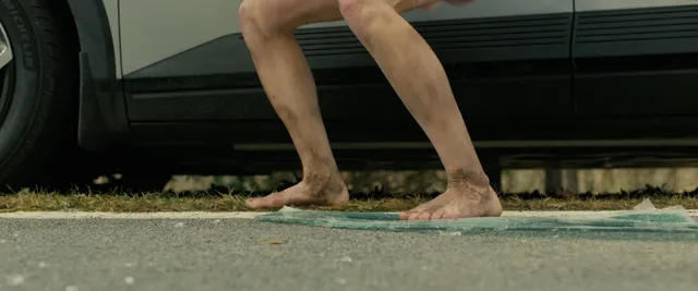 Sophie Thatcher standing barefoot beside a vehicle in a film scene.