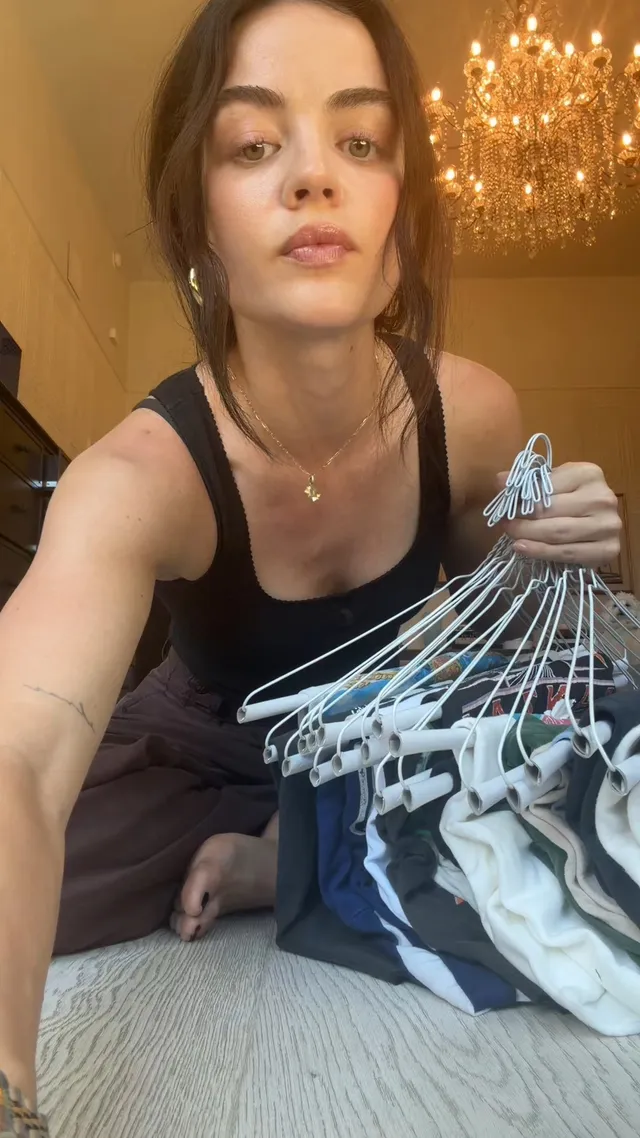 Lucy Hale sitting on a rug beside clothes hangers.
