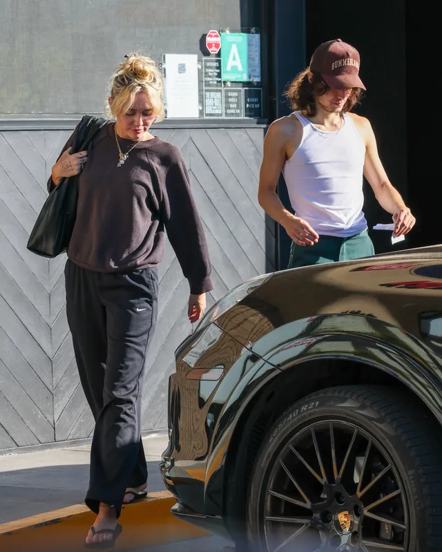 Miley Cyrus walking outside beside another woman in a dark outfit.