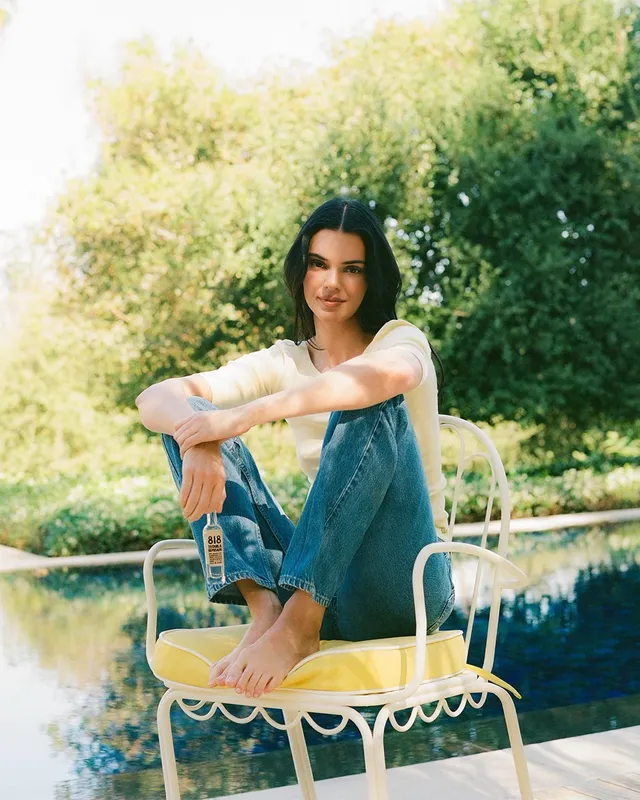 Kendall Jenner sitting barefoot on a garden chair in jeans.