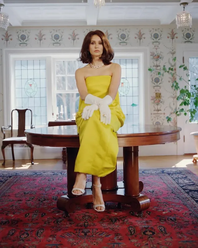 Nina Dobrev wearing a yellow dress and pale heels indoors.