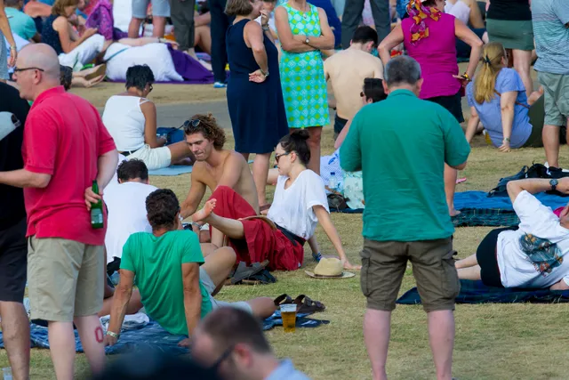 Daisy Ridley sitting among a crowd on grass in a red dress.