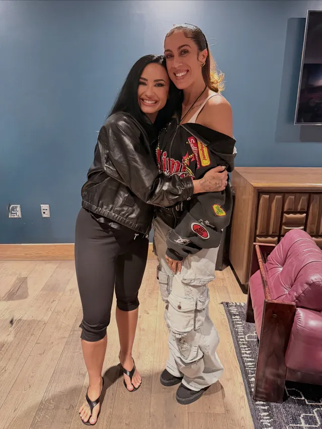Demi Lovato standing beside another person in cropped trousers and flip-flops.