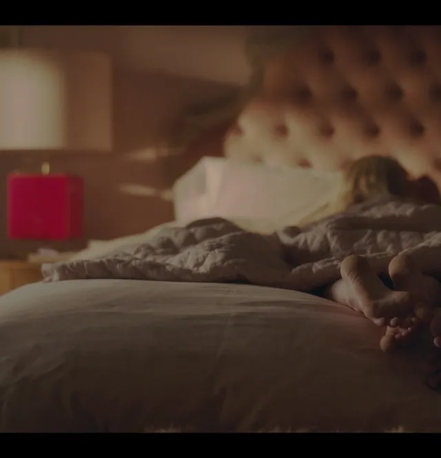 Emily Alyn Lind reclining on a bed with a bare foot visible in a screen capture.