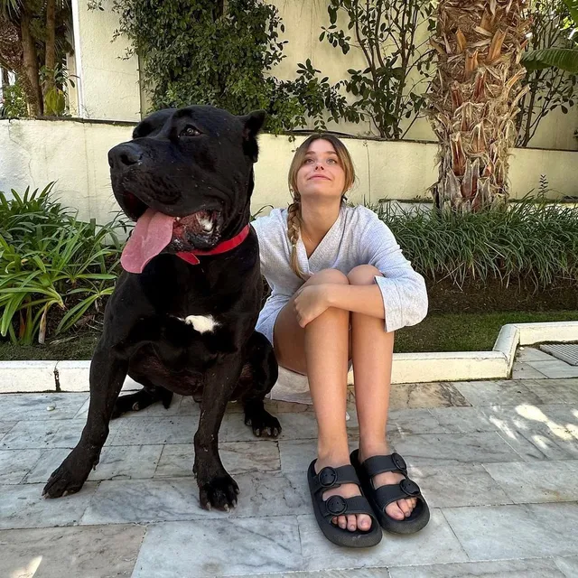 Nicole Wallace sitting outdoors beside a dog in dark flat sandals.