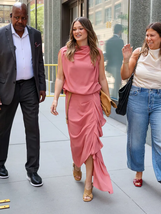 Olivia Holt walking with guests in a pink dress and gold heels.