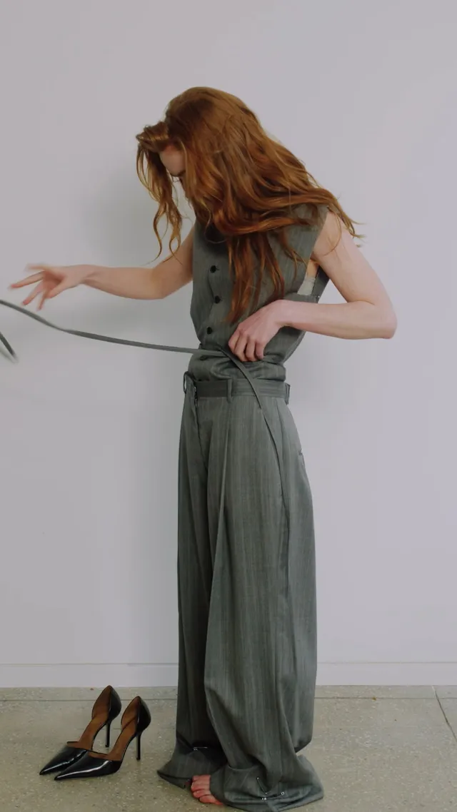 Sadie Sink posing barefoot in a gray studio outfit.