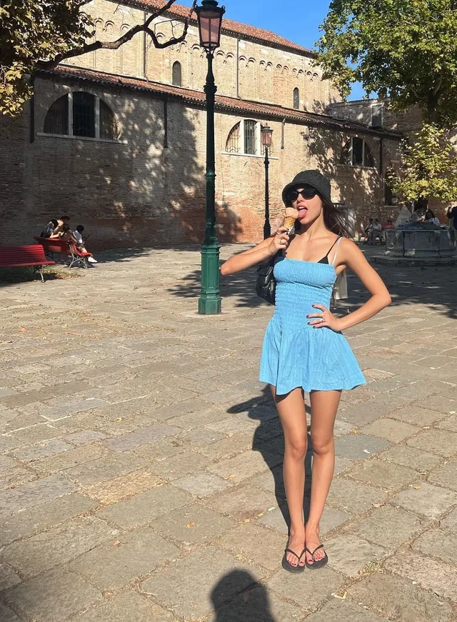 Olivia Rodrigo standing outdoors in a blue mini dress and flip flops.