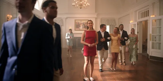 Lola Tung wearing a short red dress and pale heels in a scene.