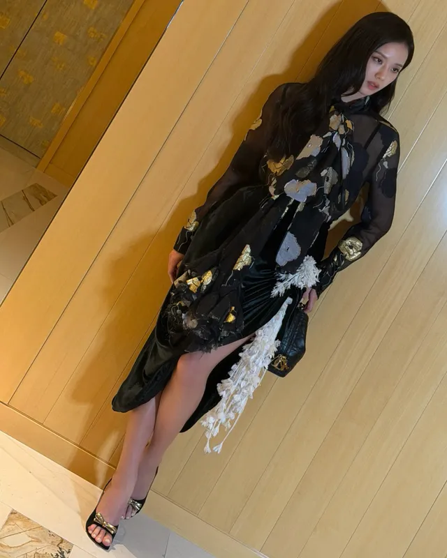 Jisoo posing in black heels and a long patterned dress indoors.