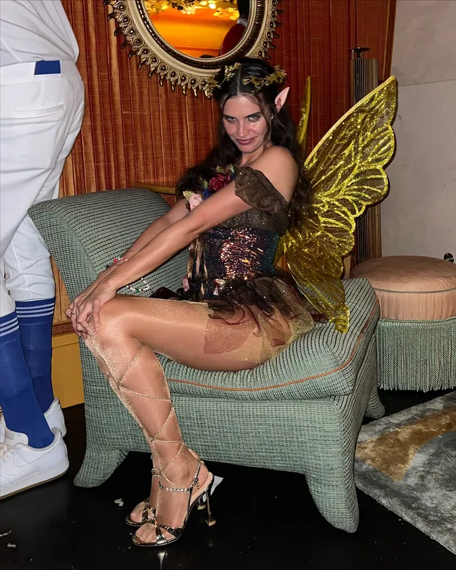 Sara Sampaio sitting in a chair in a winged costume and lace-up heels.