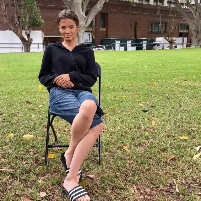 Freya Allan sitting outdoors in a blue skirt and striped slide sandals.