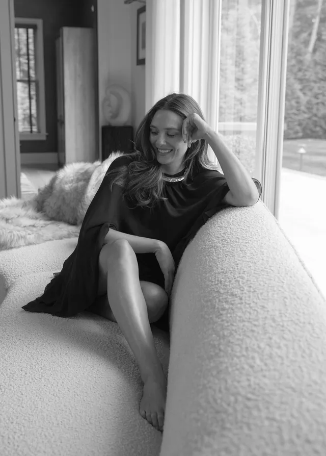 Elizabeth Olsen sitting barefoot on a rounded sofa in black and white.