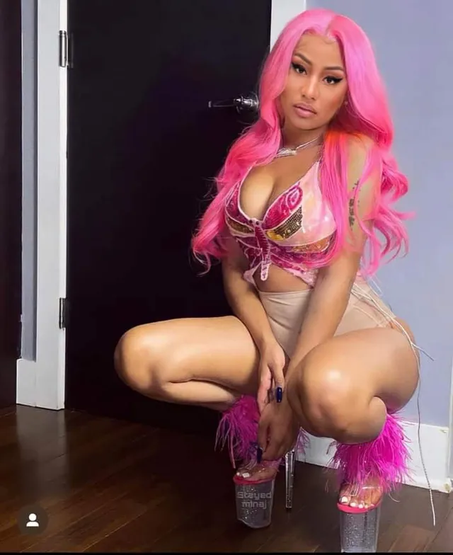 Nicki Minaj crouching indoors in feather-trimmed platform heels.