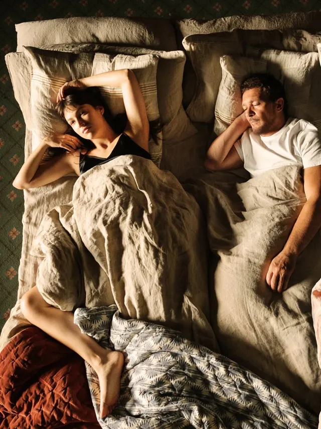 Úrsula Corberó reclining barefoot beside a man in bed in a portrait.