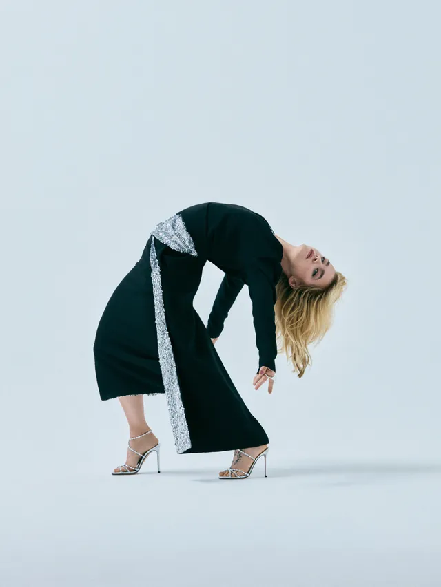 Clara Galle posing in a black outfit and metallic heels against a pale backdrop.
