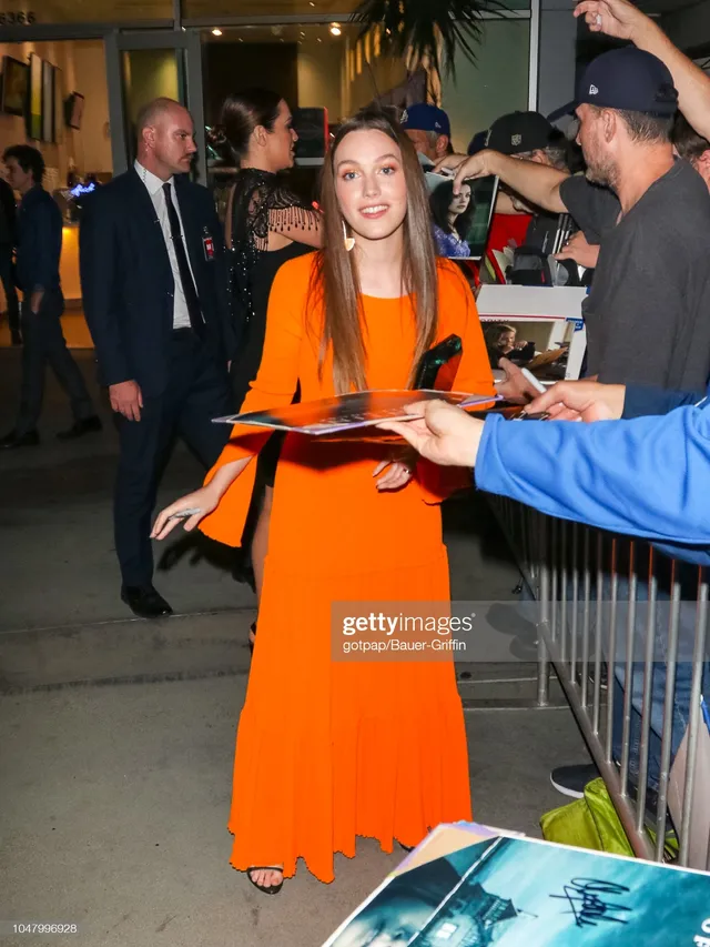 Victoria Pedretti greeting fans outside a venue in an orange dress.