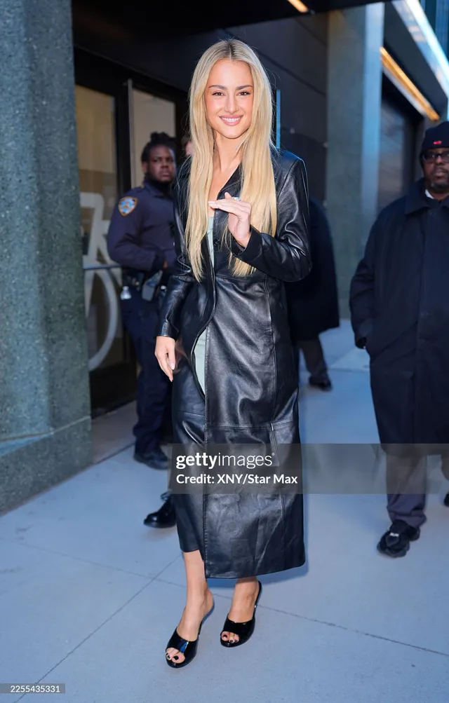 Grace Van Patten walking outside in a black leather dress and open-toe heels.