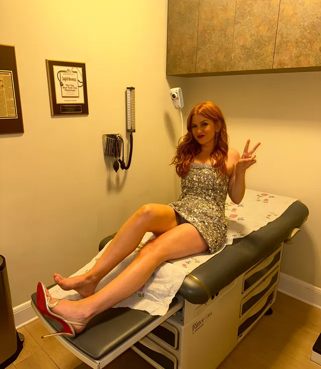 Isla Fisher sitting on an examination bed in a patterned dress.