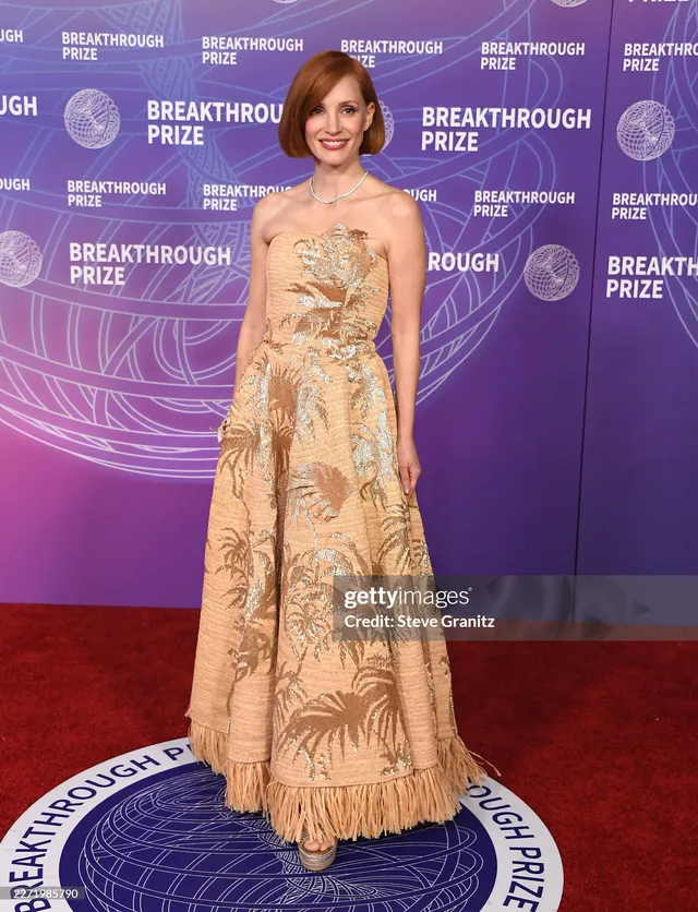 Jessica Chastain posing in a long gold gown at an awards event.