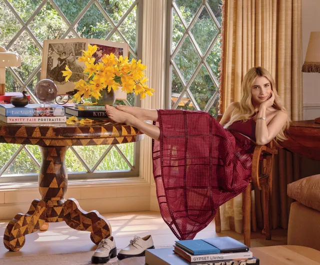 Emma Roberts reclining in a red dress with bare feet resting on a table.