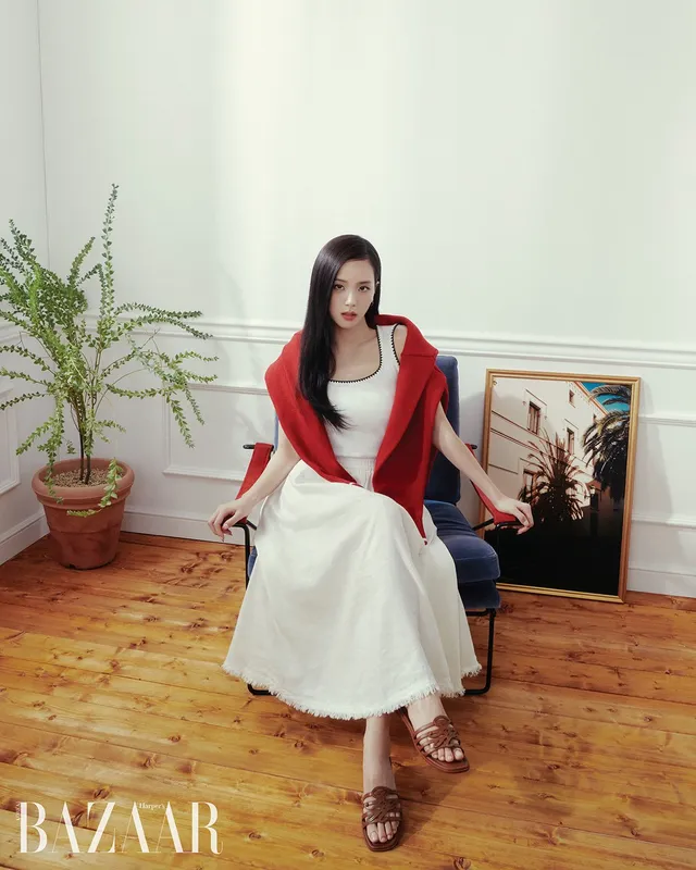 Jisoo sitting in heeled sandals and a white dress with a red jacket.