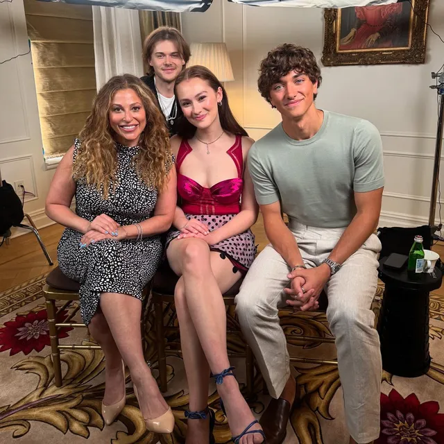 Lola Tung sitting with fellow performers in a patterned dress and strappy heels.