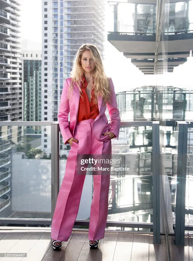 Anna Kournikova wearing black heels and a bright pink suit beside a balcony railing.