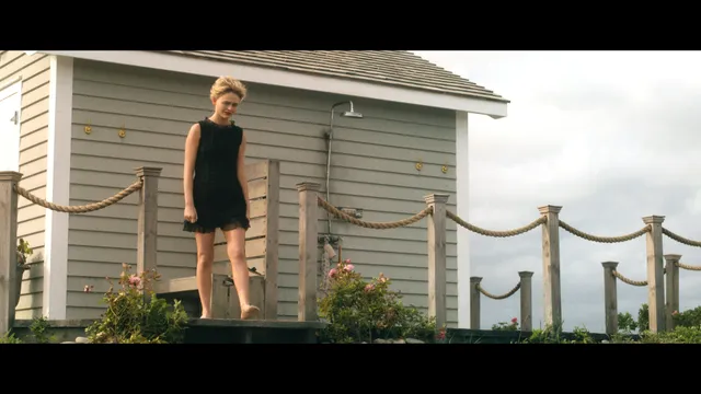 Emily Alyn Lind standing barefoot on a deck in a black dress.