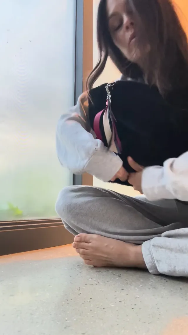 Rachel Bilson sitting cross-legged indoors holding a bag.