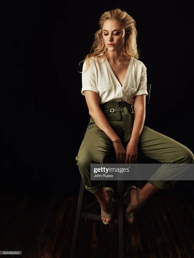 Maika Monroe sitting in cropped green trousers and heels.