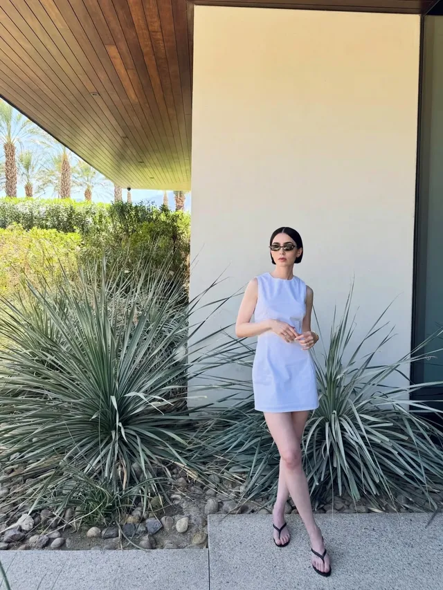 Lily Collins standing outdoors in a pale dress and flip-flops.