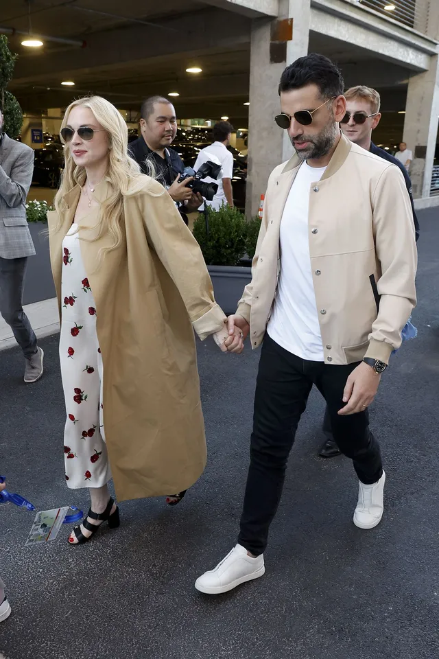 Lindsay Lohan walking outdoors in a long coat beside a companion.