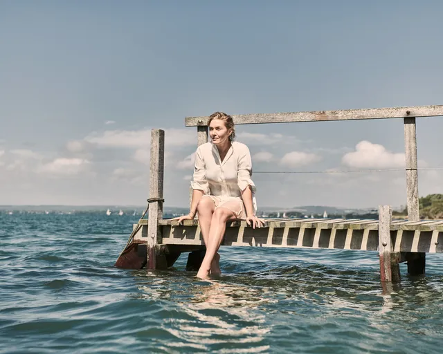 Kate Winslet sitting barefoot on a wooden pier.