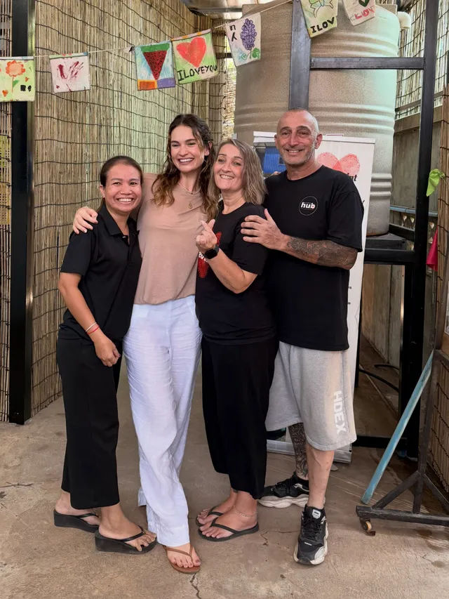 Lily James posing with a group indoors in a pink dress and sandals.
