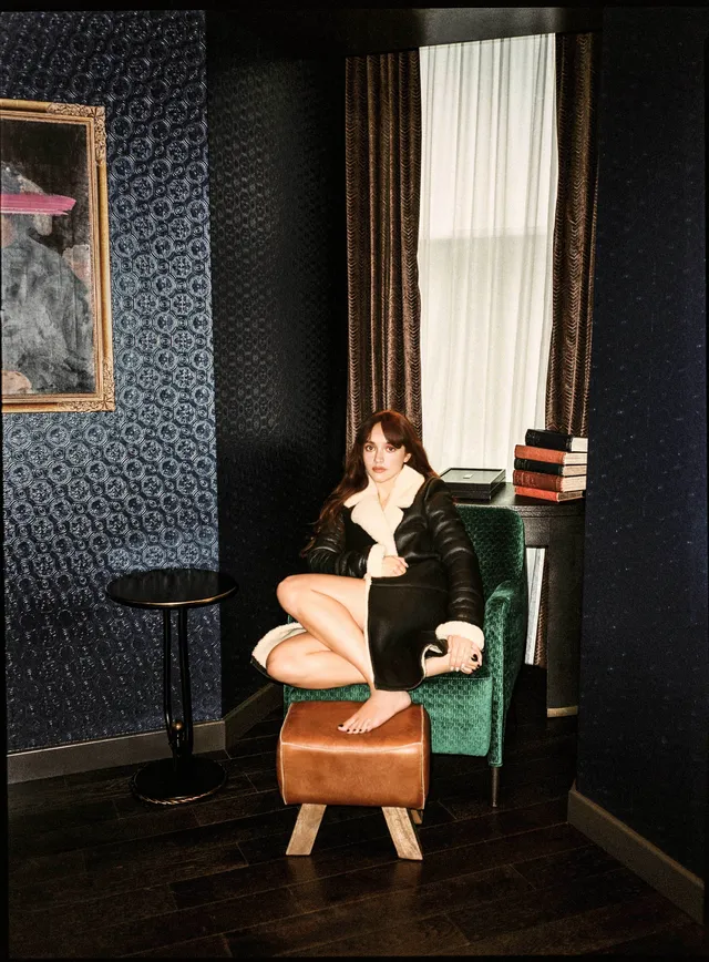 Olivia Cooke sitting in a green chair in a dark room.