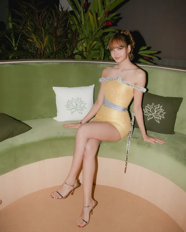 Lisa (Lalisa Manobal) sitting on a curved green sofa in pale heels and a yellow outfit.