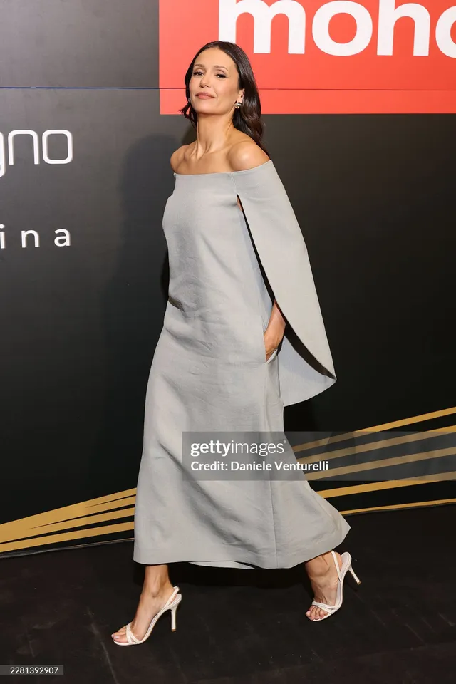 Nina Dobrev wearing a gray dress and white heels on a carpet.