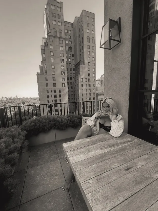 Bebe Rexha sitting on an outdoor balcony beside a table.