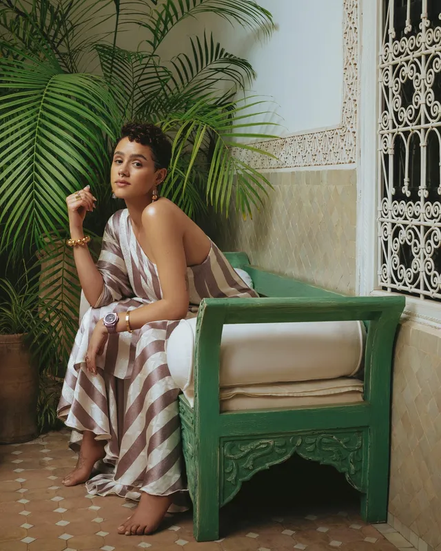 Nathalie Emmanuel sitting in a green chair on a tiled patio.